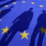 European Union flag painted on tiled street floor and shadows group of people walking at sunny day.